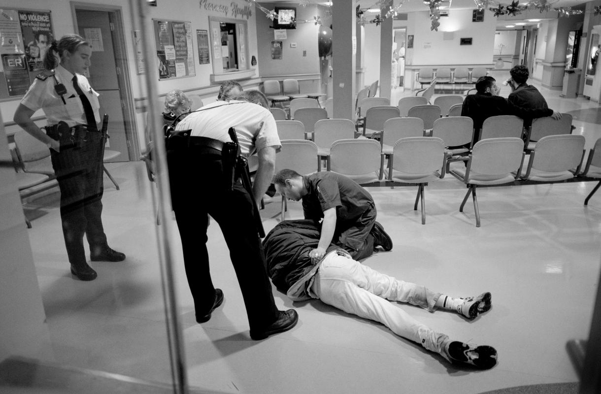 GB. WALES. Cardiff. Emergency accident area, University Hospital, a violent patient, very much the worse for drink, collapses in the waiting area and the police are called. Cardiff. 2000.